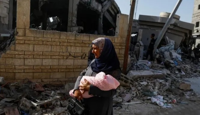 Một phụ nữ Palestine bồng con đi gần địa điểm xảy ra vụ tấn công của Israel vào nhà thờ hồi giáo ở Khan Younis, phía nam Dải Gaza.